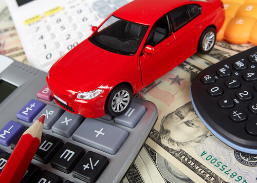 A red car on top of money and a calculator - signify the cost of auto shipping