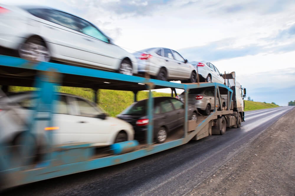 A car carrier trailer with 7 cars zooming down a rural road.